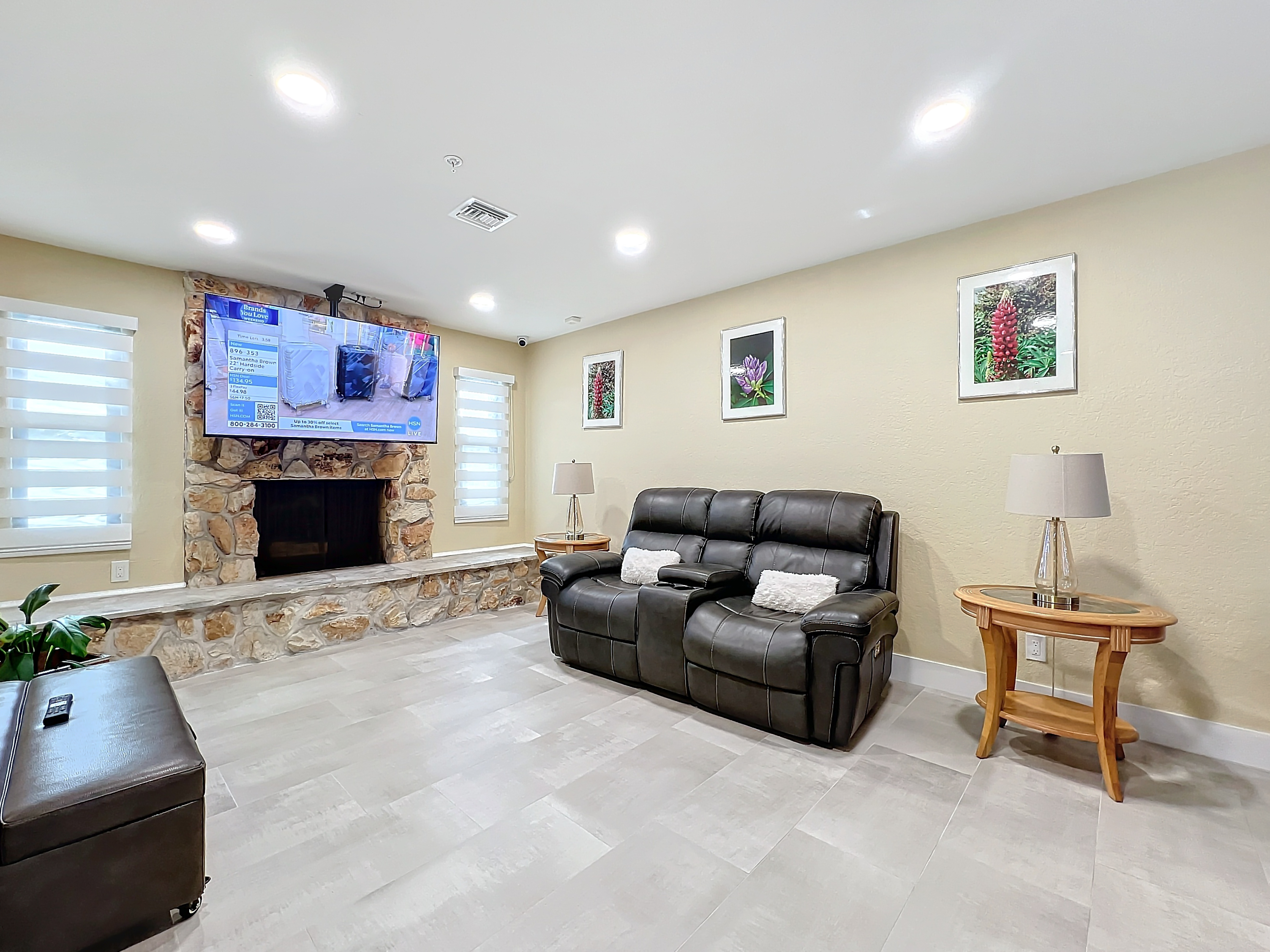 Warm living area featuring a stone fireplace, wall-mounted television, and comfortable recliners at Abundant Care Residence in Wellington, FL
