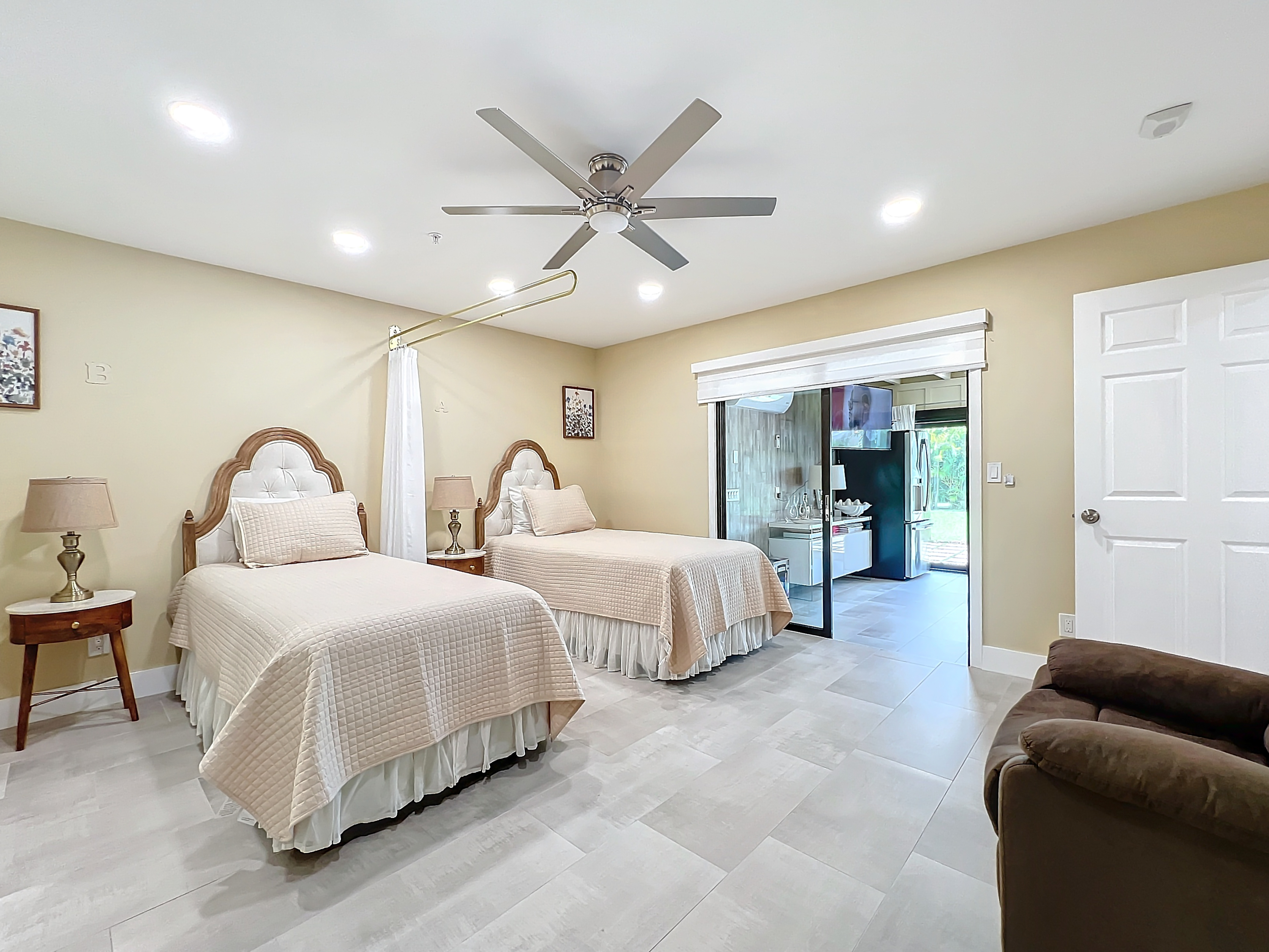 Shared resident room with two beds, privacy curtain, recliner, and sliding glass door patio access at Abundant Care Residence in Wellington, FL