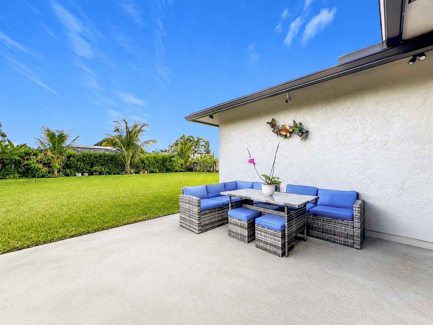 Beautiful backyard patio with comfortable wicker furniture and tropical landscaping at Abundant Care Residence in Wellington, FL